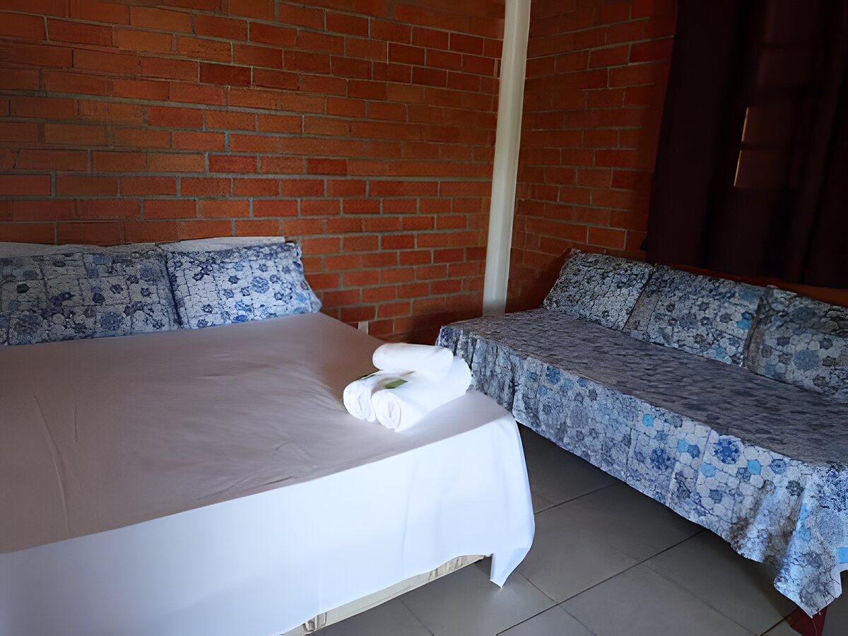 Quarto com cama de casal e sofá-cama, parede de tijolo aparente