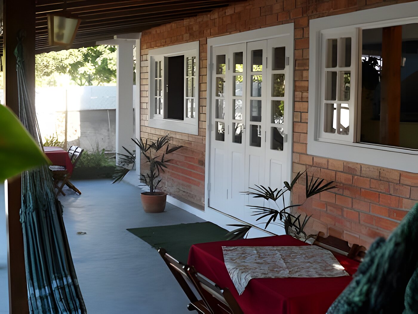 Varanda da pousada com redes, mesa e vegetação ao redor
